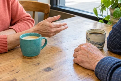 ידיה של אישה בוגרת לצד ידיו של גבר בוגר סביב שני ספלי קרמיקה במהלך שיחה בבית קפה מואר